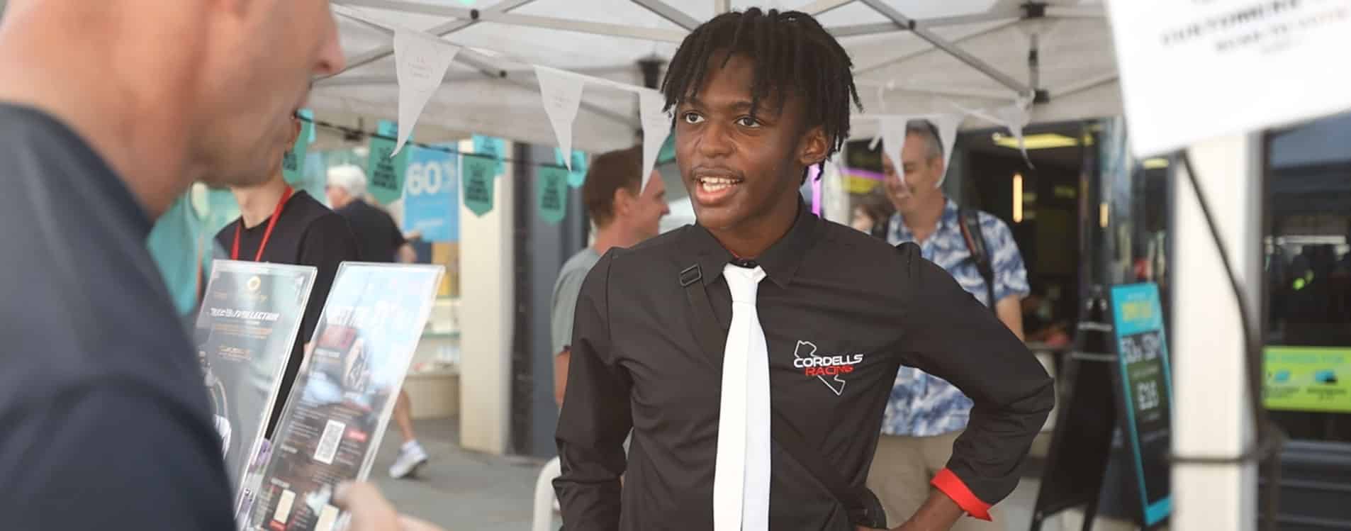Young entrepreneur in a branded shirt chats to customer at the Young Business Showcase